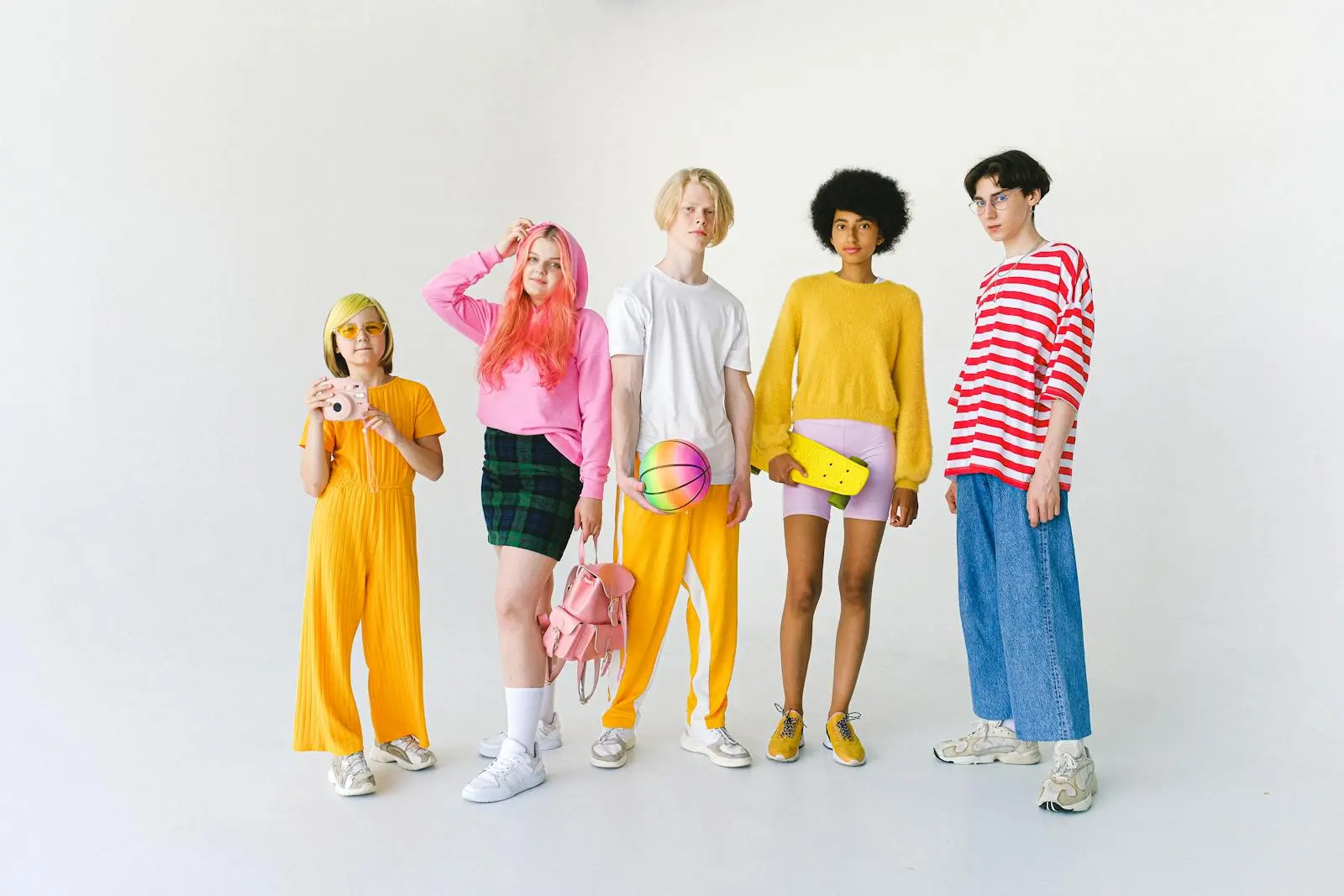 A vibrant group of teenagers in colorful outfits posing with various accessories in a studio setting.